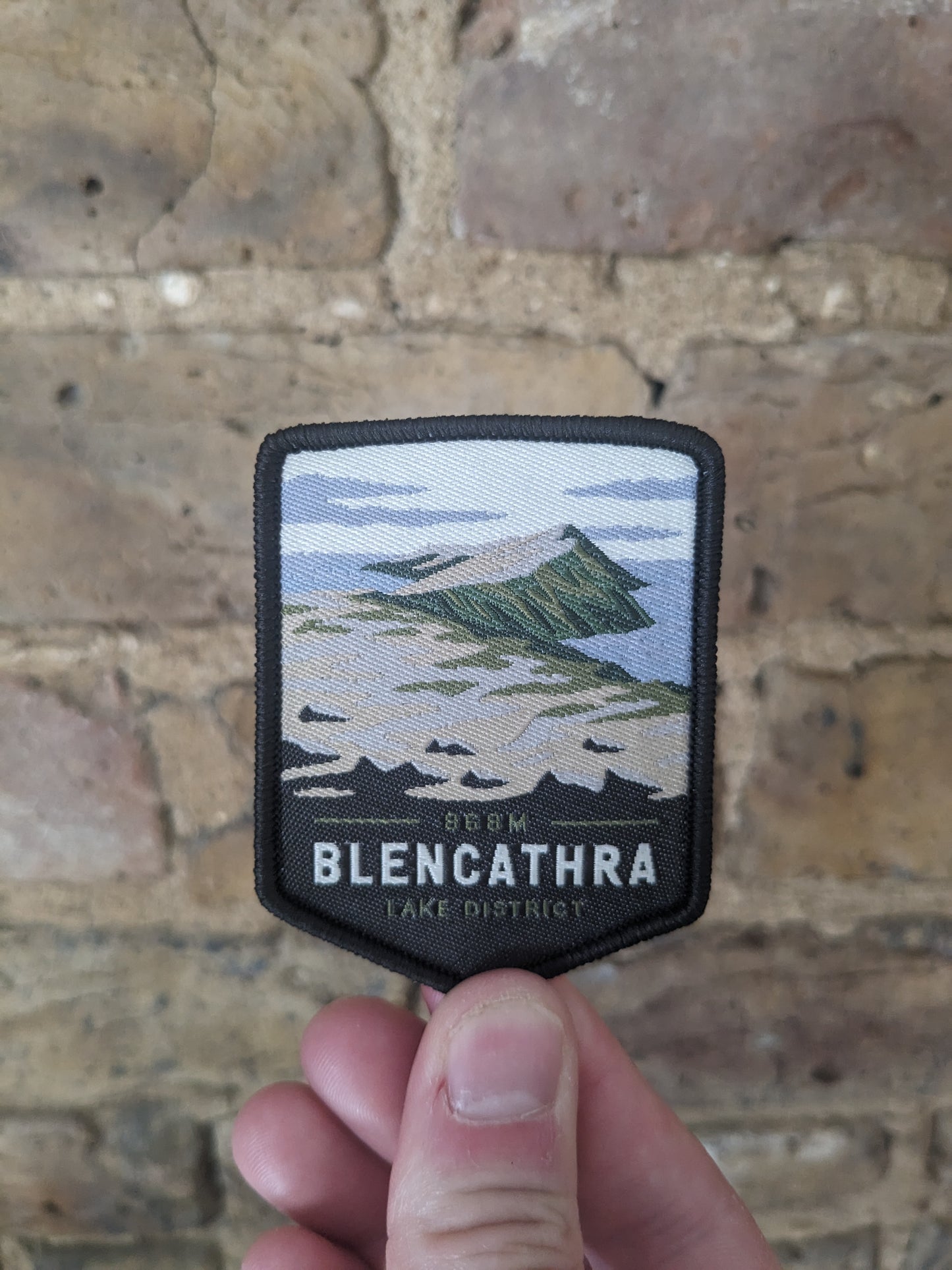 Image of the Blencathra badge being held up against a brick wall backdrop.