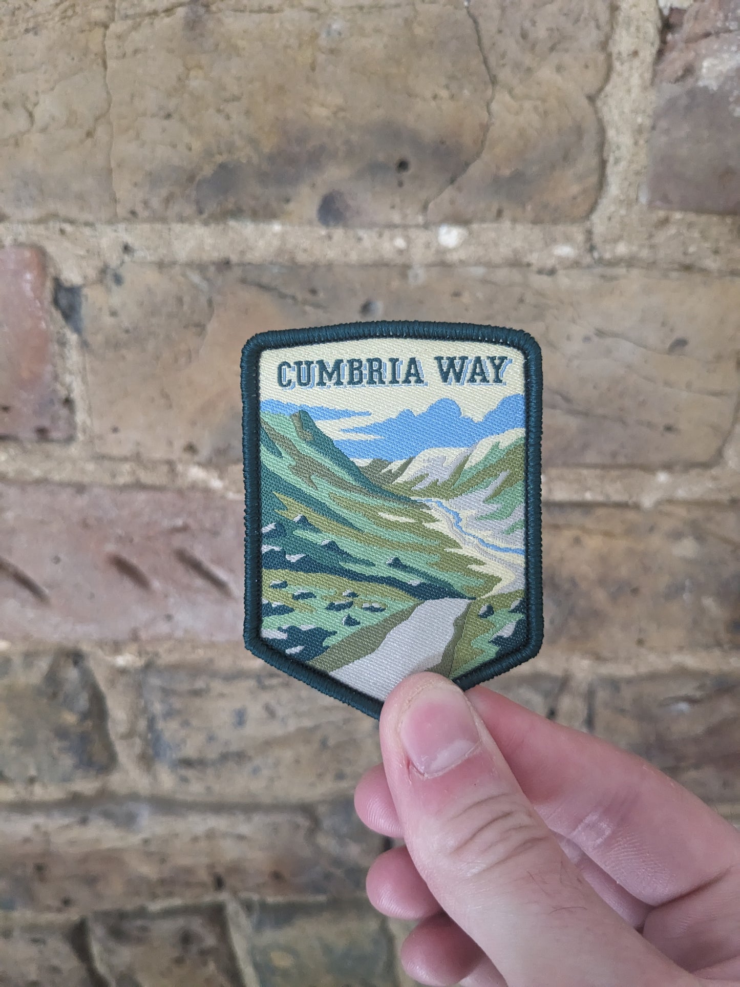 Image of the Cumbria Way patch being held against a brick wall.